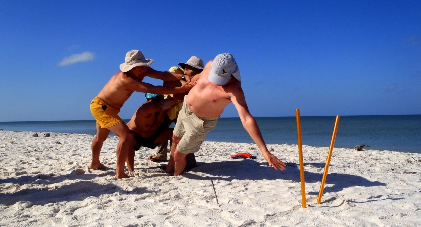 A few people brace another as they participate in a team building exercise on a beach. 